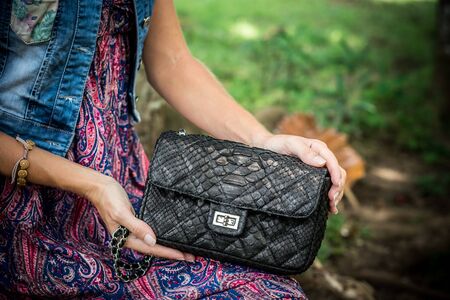 Portrait of a Beautiful fashionable caucasian brunette woman with sunglasses and luxury snakeskin python handbag posing in the park of Nusa Dua, Bali, Indonesia. Asia. Sunny day, green background.の写真素材