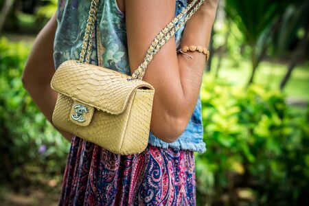 Portrait of a Beautiful fashionable caucasian brunette woman with sunglasses and luxury snakeskin python handbag posing in the park of Nusa Dua, Bali, Indonesia. Asia. Sunny day, green background.の写真素材