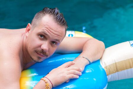 Portrait of handsome smiling man on the inflatable mattress in swimming pool at sunny day. Bali.の写真素材