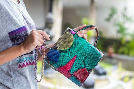 Stylish summer woman holding luxury snakeskin python handbag. Beautiful colors. Woman hands with bag.の写真素材
