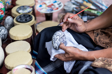 Close up on the hand of an artist with a paint brush, painting buddha on egg. Tropical Bali island, Indonesia.の写真素材