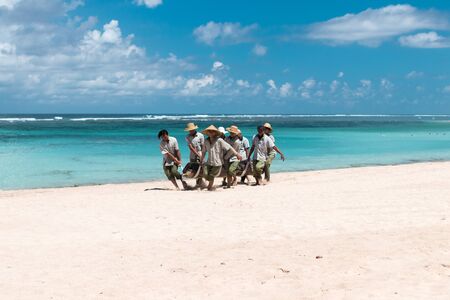 BALI, INDONESIA - APRIL 26, 2017: Paradise beach workers bringing a big tree on Bali island, Indonesia.のeditorial素材