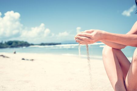 Sand as the time slips through your fingers. Girl holding a sand sea background. Concept of vacation in warmer climes, the trip to the sea. Bali island, Indonesia.の写真素材