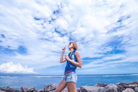 Beautiful young woman blowing bubble in outdoor, nature, near the ocean. Tropical magic island Bali, Indonesia.の写真素材