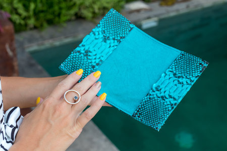 Luxury snakeskin python blank passport cover in woman hands. Bali, swimming pool.