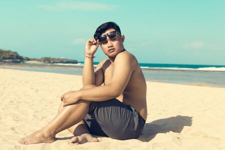 Young asian indonesian man on the beach of tropical Bali island, Indonesia.の写真素材