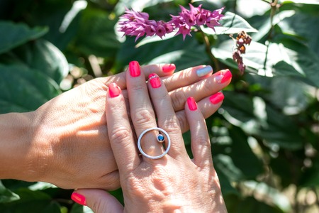 Closeup of hands of a young woman with red manicure on nails against natural green tropical background.の写真素材