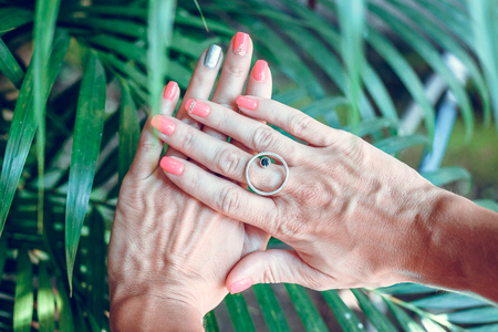 Closeup of hands of a young woman with red manicure on nails against natural green tropical background.の写真素材