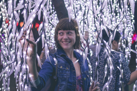Closely image of young woman among christmas garlands lights. Bali light festival, Indonesia.