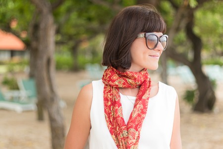 Beauty portrait of sexy brunette woman in white dress on the beach with colorful silk scarf and sunglasses. Cruise summer fashion. Bali, Indonesia.の写真素材