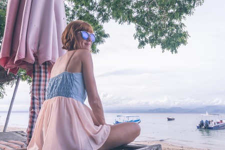 Woman sitting on beach in deck chair on a cloudy day. Nusa Lembongan island, Bali, Indonesia.の写真素材