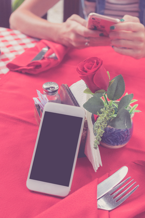 Mockup image of white mobile phone with blank white screen on red background in restaurant. Tropical Bali island, Indonesia. Woman hands with smartphone on blurred background.の写真素材