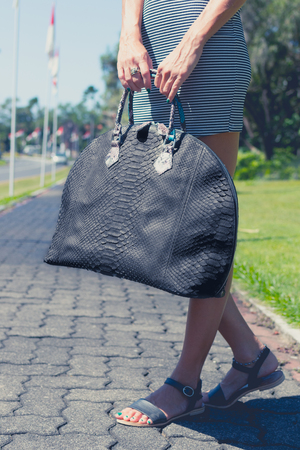 Woman with a big luxury snakeskin fashion python bag in the park of Nusa Dua, Bali island.の写真素材