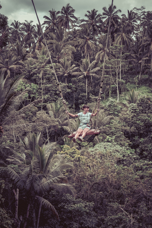 Young tourist woman swinging on the cliff in the jungle rainforest of a tropical Bali island.の写真素材