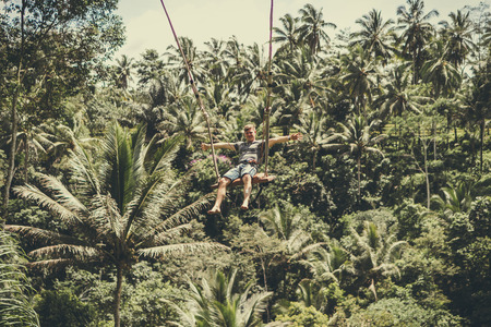 BALI, INDONESIA - DECEMBER 5, 2017: Young tourist man swinging on the cliff in the jungle rainforest of a tropical Bali island, Indonesia.のeditorial素材