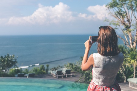 Young woman taking photos on the cliff with a beautiful ocean background at sunny day. Bali island.の写真素材