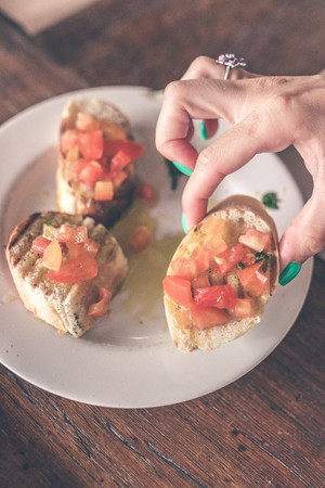 Closeup woman hand holding bruschettas on a wooden background. Italian restaurant.の写真素材