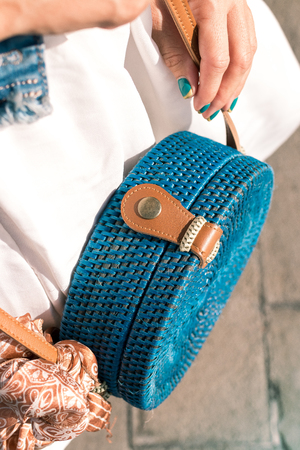 Woman hands with fashionable stylish blue rattan bag and silk scarf outside. Tropical island of Bali, Indonesia. Rattan handbag and silk scarf.の写真素材