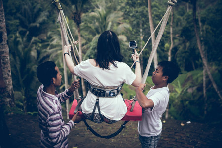 BALI, INDONESIA - DECEMBER 26, 2017: Woman having fun a swing in the jungle. Woman swinging in the...