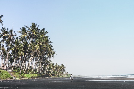 Young woman driving a scooter at the beach with black sand. Bali island.の写真素材