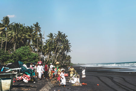 BALI, INDONESIA - MAY 19, 2018: Balinese Hindu devotees with offerings for the spirits of the sea walking to the beach. Black sand beach ceremony.のeditorial素材