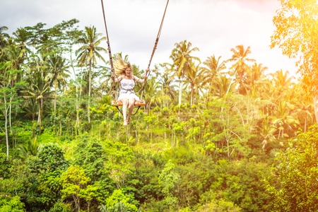 Young tourist woman swinging on the cliff in the jungle rainforest of a tropical Bali island. Indonesian swing.の写真素材