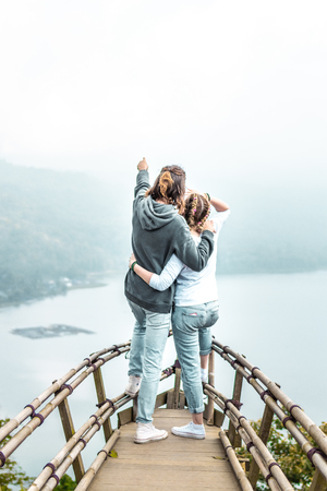 Happy young couple of tourists on the wooden bridge with tropical background. Lake. Bali island.の写真素材