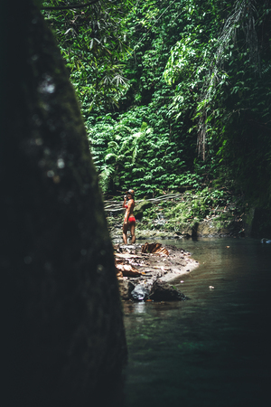 Rear view of young woman tourist with straw hat and red swimsuit in the deep jungle. Real adventure concept. Bali island.の写真素材