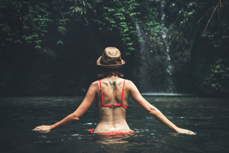 Young woman tourist with straw hat in the deep jungle with waterfall. Real adventure concept. Bali island.の写真素材