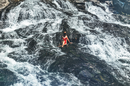 Young woman in red swimsuit on cascade waterfall on Bali island.の写真素材