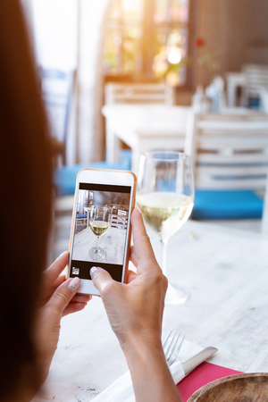 Woman taking photo of white wine on her smartphone in restaurant. Bali island.の写真素材