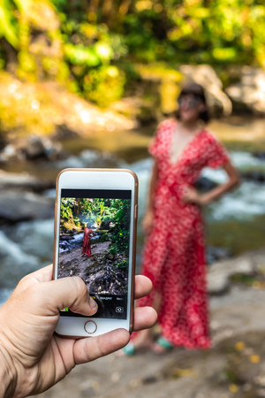 Man taking photo of woman in long red dress in nature of Bali island.の写真素材