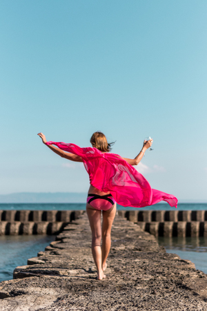 Young woman in a long red dress and with a glass of wine posing on the sea background. Bali island.の写真素材