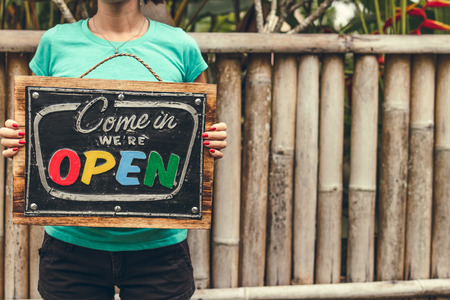 Open sign board in woman hands. Bali island background.の写真素材