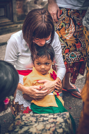 BALI, INDONESIA - DECEMBER 26, 2018: European woman with balinese kid on a traditional ceremony.のeditorial素材