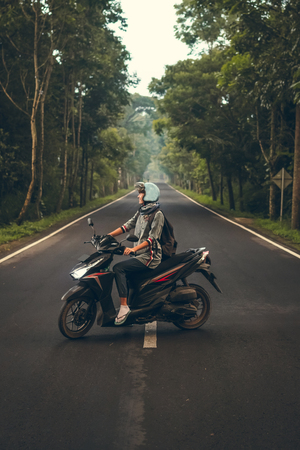 Young woman on the scooter on the road among the trees. Bali island.の写真素材