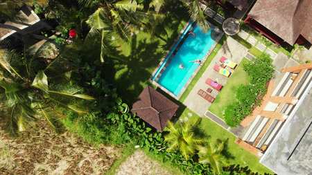 BALI, INDONESIA - DECEMBER 27, 2018: Group of friends having fun in swimming pool outdoors. 4K flying drone video.のeditorial素材