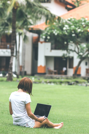 Woman online shopping concept. Woman in the green park with modern laptop. Bali island. Indonesia.の写真素材