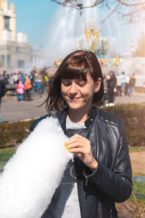 Close up portrait of a smiling excited girl holding cotton candy in the park close to fountain.の写真素材