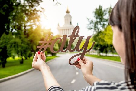 Letters city in woman hand on a city background. Hashtag city.の写真素材
