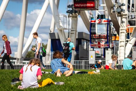 MOSCOW, RUSSIA - AUGUST 25, 2019: People relaxing on the lawn on Ferris Wheel background.のeditorial素材