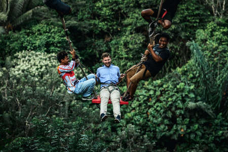 BALI, INDONESIA - MAY 16, 2018: Young man swinging in the jungle rainforest of Bali island, Indonesia. Swing in the tropics. Swings - trend of Bali island.のeditorial素材
