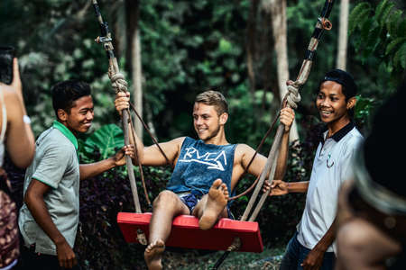 BALI, INDONESIA - MAY 16, 2018: Young man swinging in the jungle rainforest of Bali island, Indonesia. Swing in the tropics. Swings - trend of Bali island.のeditorial素材