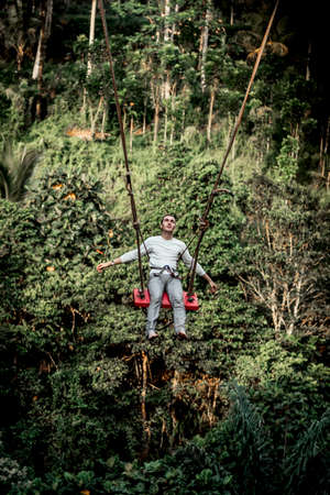 BALI, INDONESIA - MAY 16, 2018: Young man swinging in the jungle rainforest of Bali island, Indonesia. Swing in the tropics. Swings - trend of Bali island.のeditorial素材