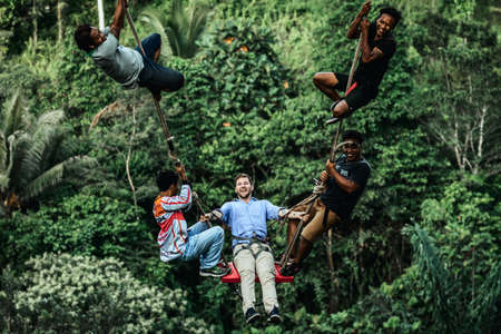 BALI, INDONESIA - MAY 16, 2018: Young man swinging in the jungle rainforest of Bali island, Indonesia. Swing in the tropics. Swings - trend of Bali island.のeditorial素材