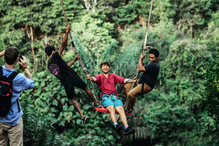BALI, INDONESIA - MAY 16, 2018: Young man swinging in the jungle rainforest of Bali island, Indonesia. Swing in the tropics. Swings - trend of Bali island.のeditorial素材