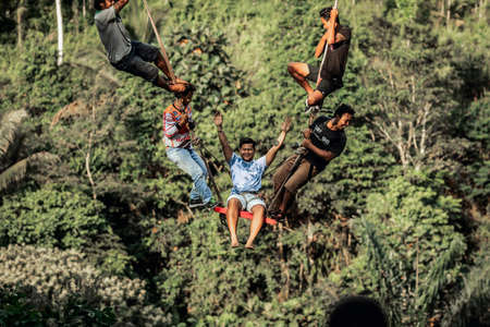 BALI, INDONESIA - MAY 16, 2018: Young man swinging in the jungle rainforest of Bali island, Indonesia. Swing in the tropics. Swings - trend of Bali island.のeditorial素材