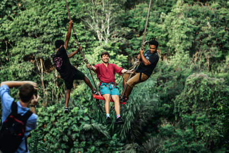 BALI, INDONESIA - MAY 16, 2018: Young man swinging in the jungle rainforest of Bali island, Indonesia. Swing in the tropics. Swings - trend of Bali island.のeditorial素材