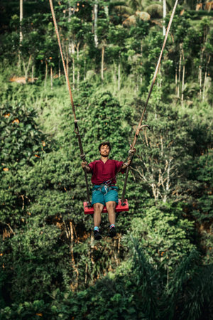 BALI, INDONESIA - MAY 16, 2018: Young man swinging in the jungle rainforest of Bali island,...