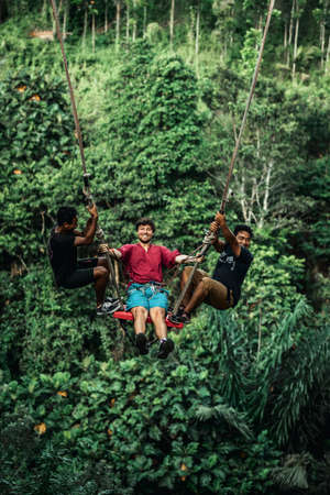 BALI, INDONESIA - MAY 16, 2018: Young man swinging in the jungle rainforest of Bali island, Indonesia. Swing in the tropics. Swings - trend of Bali island.のeditorial素材